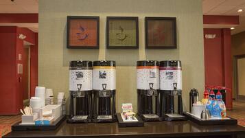 Una estación de café con cuatro máquinas de café, vasos desechables y un dispensador de bebidas.