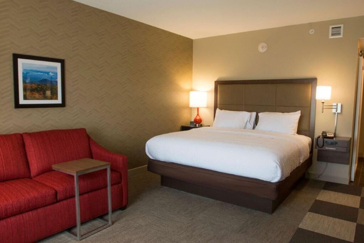 A hotel room with a bed, a red sofa, a small table, two bedside lamps, and a framed picture on the wall.