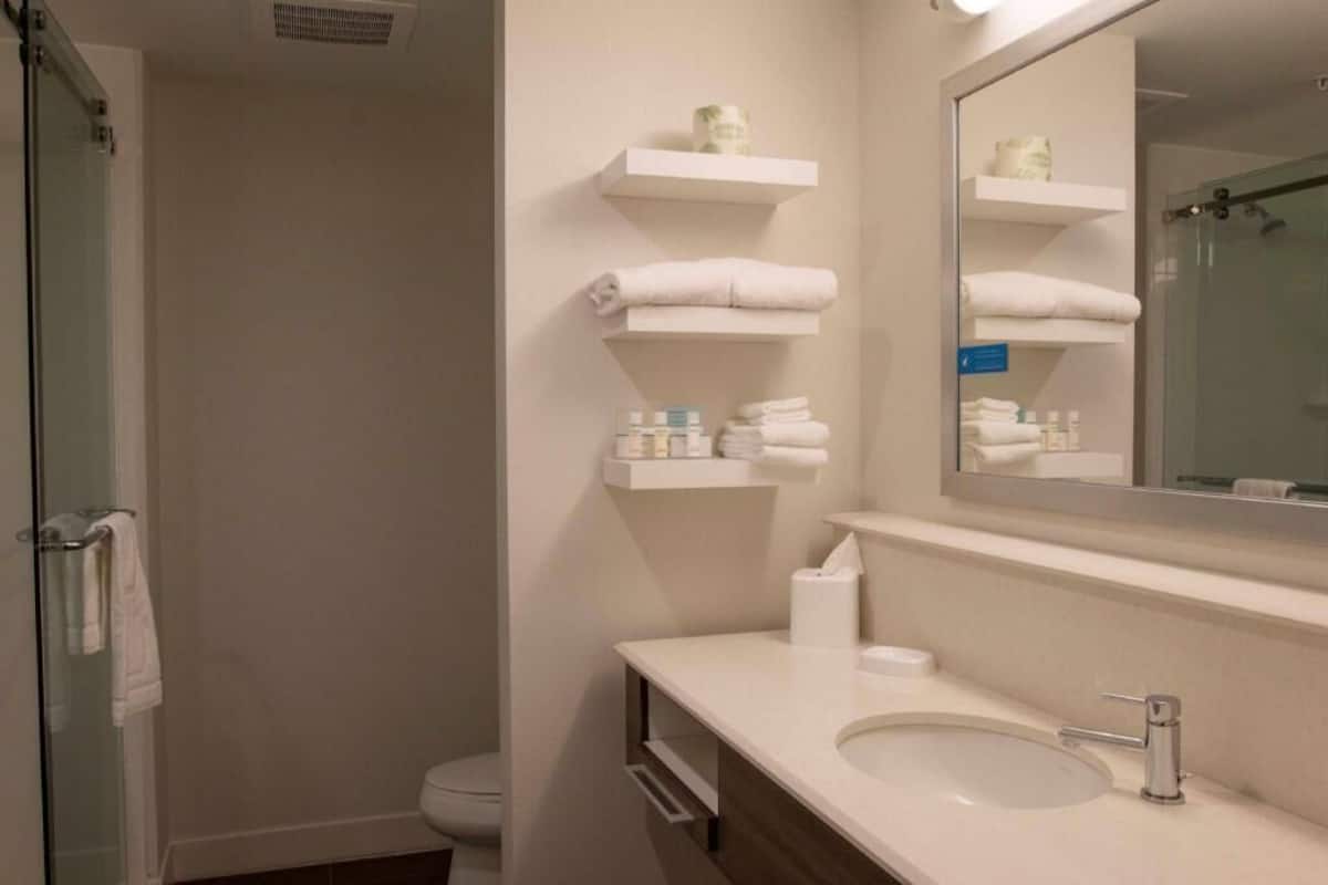 A bathroom with a sink, mirror, towel racks, and a shower.