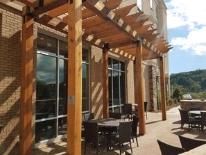 An outdoor patio with wooden pergola, brick walls, and large windows.