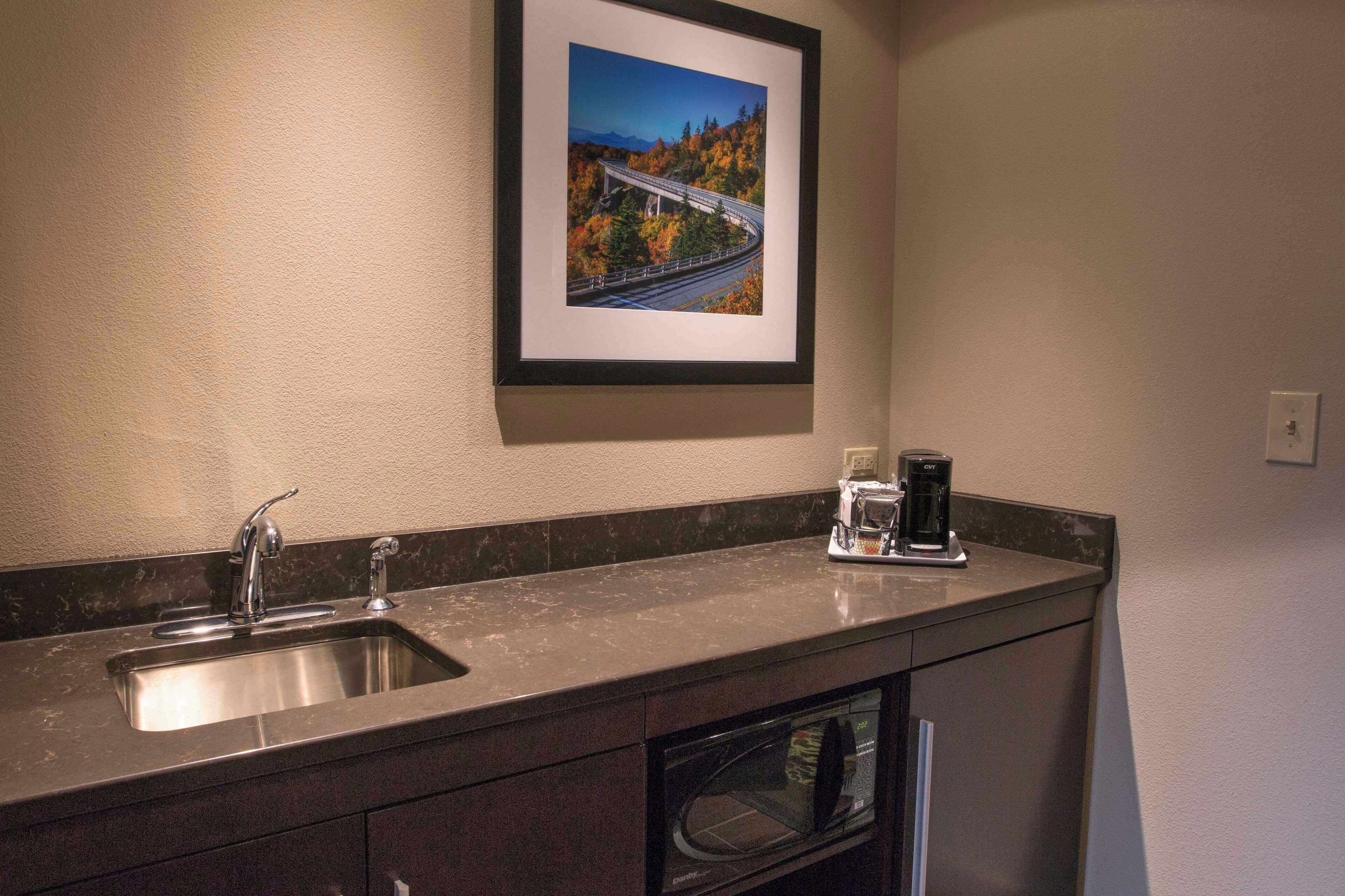 A kitchen with a double sink, a coffee maker, and a framed picture of a bridge.