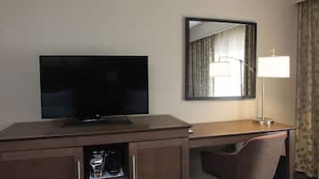 Ein Hotelzimmer mit Flachbildfernseher auf einem Holztisch, einem Spiegel, einer Schreibtischlampe und einem Stuhl.