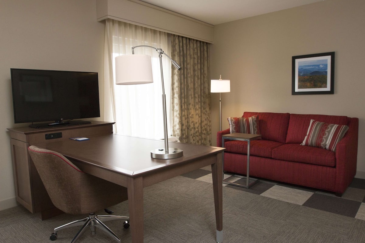 A hotel room with a desk, chair, television, red sofa, and a framed picture on the wall.