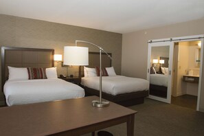 A hotel room with two beds, a desk, a lamp, and a mirror.