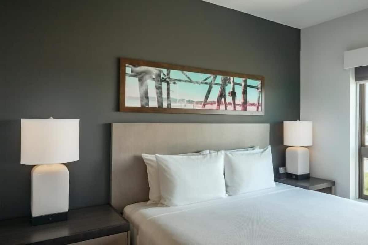 Una camera d'albergo con un letto, due lampade da comodino, un quadro appeso al muro e una finestra con vista.