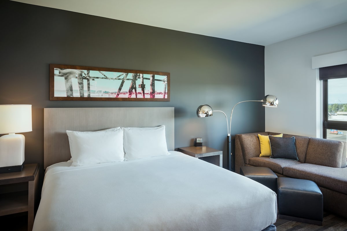 Una camera d'albergo con un letto grande, un divano, un comodino con una lampada e un quadro appeso al muro.