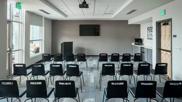 A conference room with rows of chairs, a projector, and a large screen on the wall.