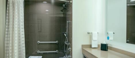 A modern bathroom with a bathtub, shower, and handrails.