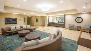 Eine geräumige Lobby mit Empfangstresen, einer Sitzecke mit Sofas und Poufs sowie einem gemusterten Teppich.