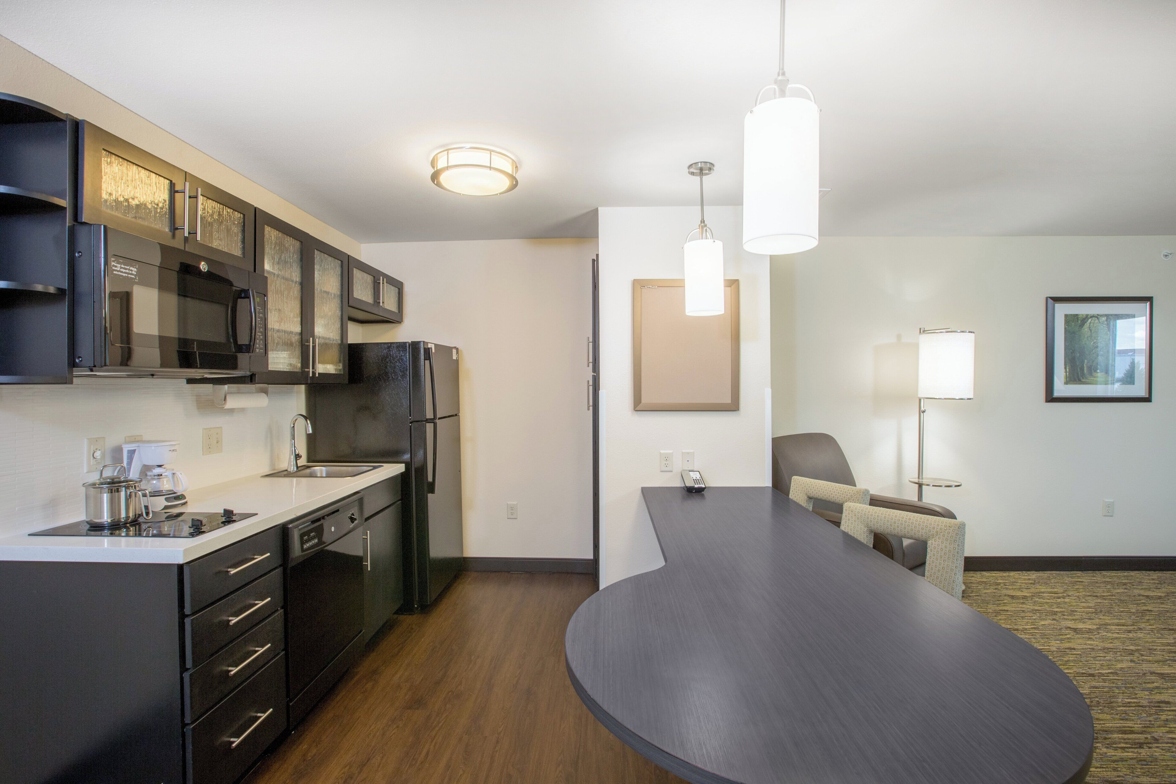 A modern kitchen with a built-in microwave, refrigerator, and coffee maker. There is a dining area with a long table and chairs.