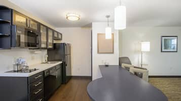 A modern kitchen with a built-in microwave, refrigerator, and coffee maker. There is a dining area with a long table and chairs.