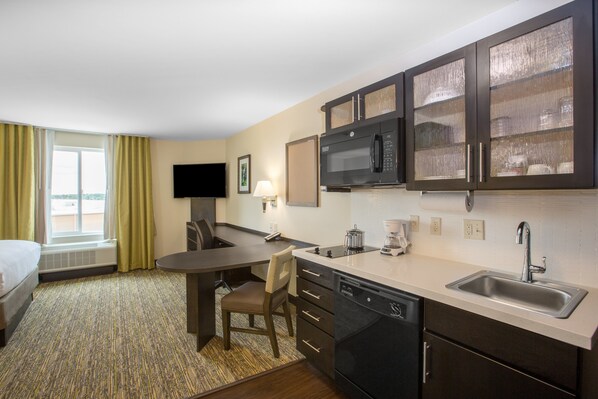 Een hotelkamer met een kitchenette, een bed, een bureau en een televisie.