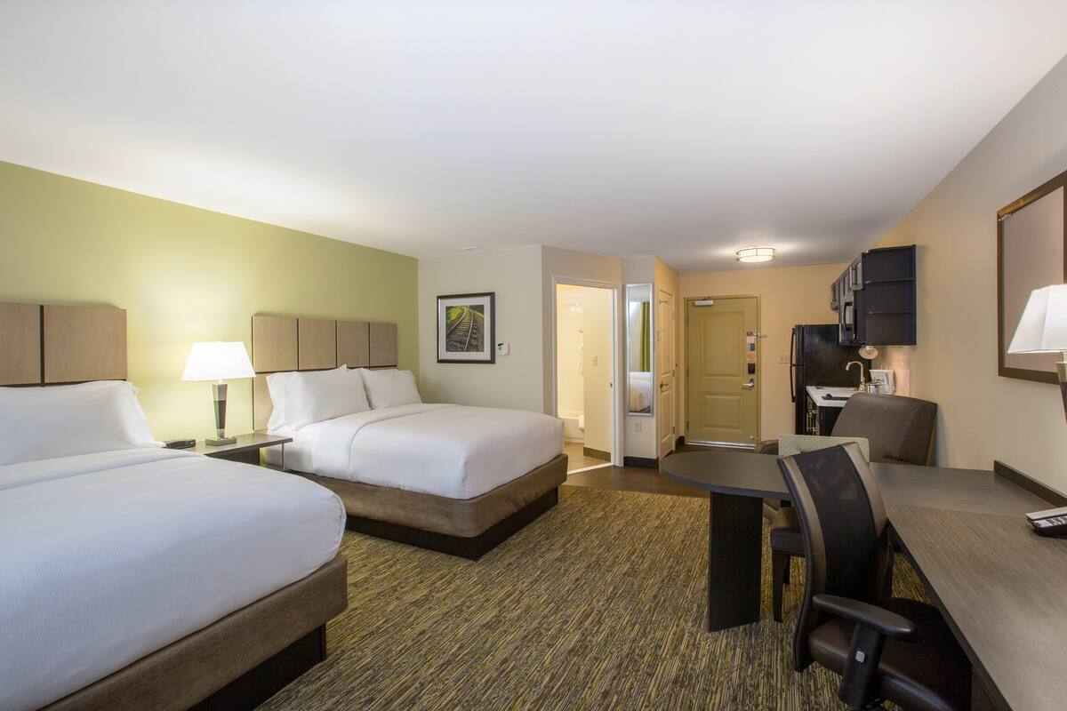 A hotel room with two beds, a desk, and a kitchenette.