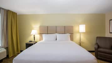 A hotel room with a large bed, two bedside lamps, a brown armchair, and a window with curtains.