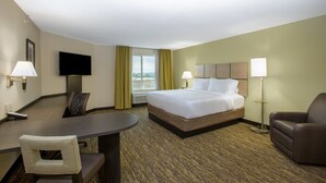 Ein Hotelzimmer mit Bett, Schreibtisch, Stuhl, Fernseher und einem Fenster mit Vorhängen.