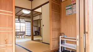 A traditional Japanese room with tatami flooring, a wooden sliding door, a small shelf with shoes, and a bench in the background. - Kyo no Yado Jorinji (Kyoto)