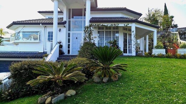 A modern house with a covered porch, a large front door, and a well-maintained lawn with various plants. - Lush & Co Auckland Bed & Breakfast (Auckland)