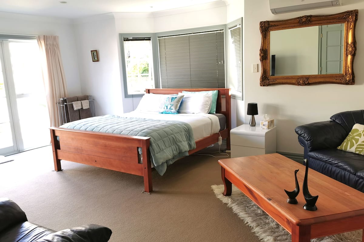 A bedroom with a wooden bed, a nightstand, a black leather sofa, and a wooden coffee table.