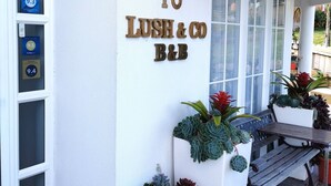 A building with a white exterior, a number '18' sign, and a 'LUSH & CO B&B' sign. There are potted plants and a bench outside. - Lush & Co Auckland Bed & Breakfast (Auckland)