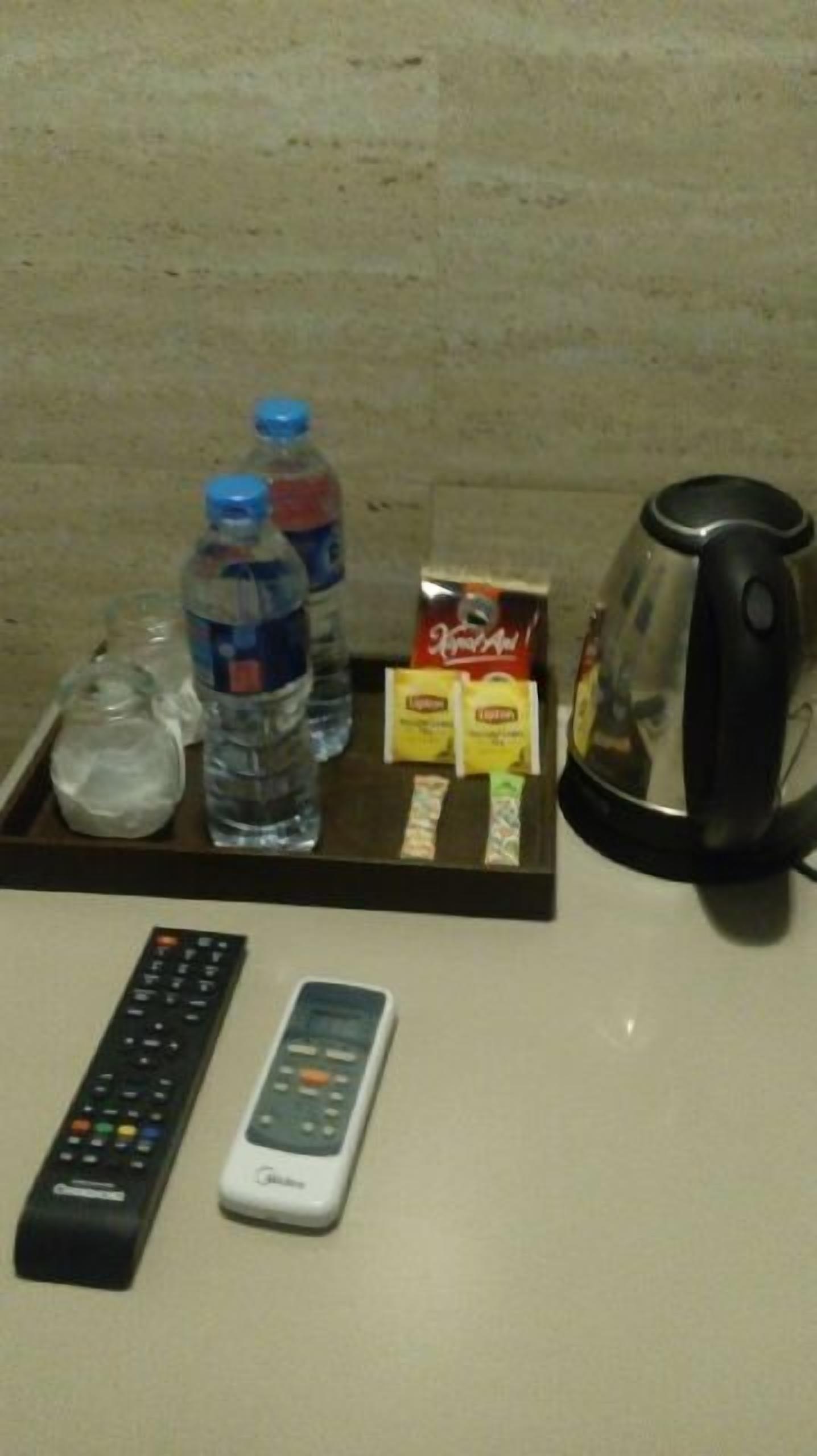Un plateau avec une bouteille d’eau, un verre, une boîte de mouchoirs Kleenex, une boîte de serviettes en papier, une télécommande et une machine à café.