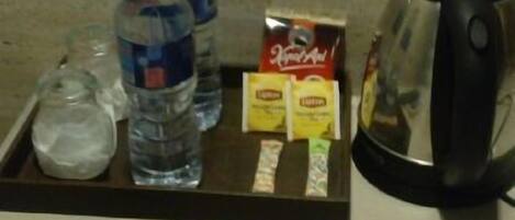 A tray with a water bottle, a glass, a box of Kleenex, a box of tissues, a remote control, and a coffee maker.