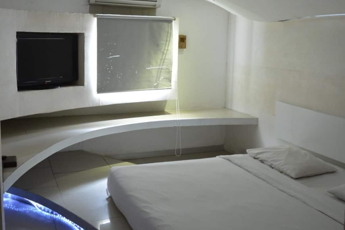 A modern bedroom with a curved bench, a bed, a TV, and a window with a view.