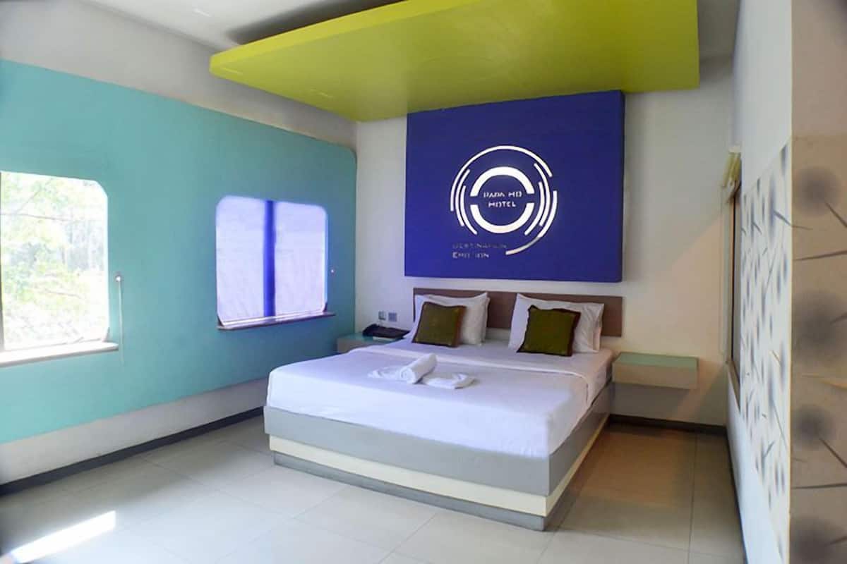 A modern hotel room with a large bed, a blue accent wall, and a logo on the wall.