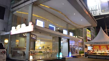 A Papa Hotel with a glass facade, visible interior seating, and a fruit stand outside.