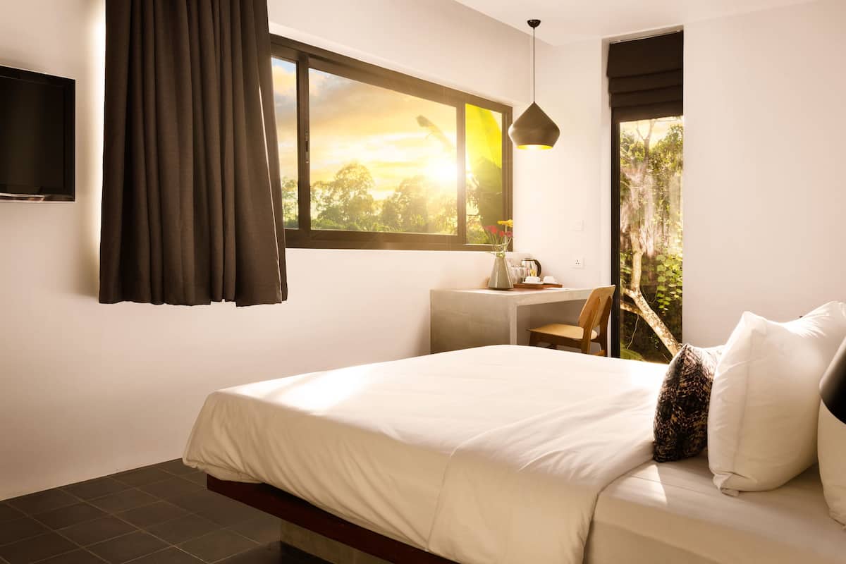 A bedroom with a bed, a desk, a chair, a TV, and a window with curtains.
