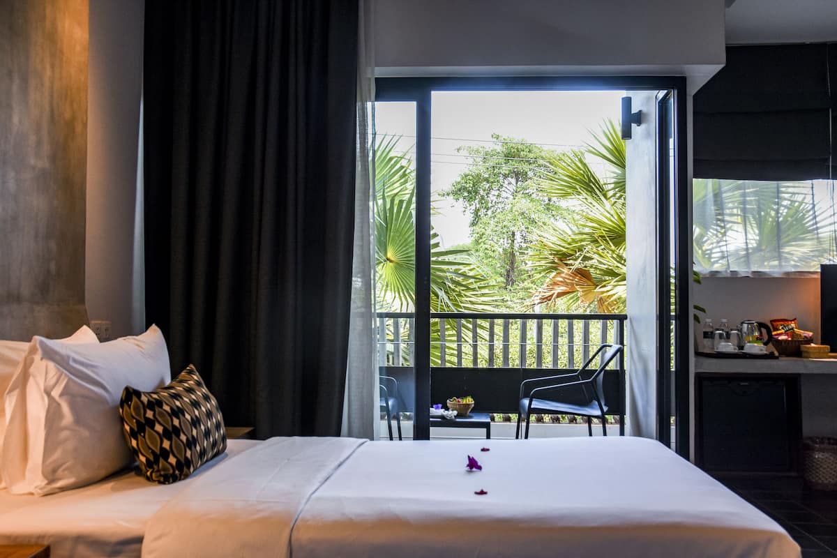 A hotel room with a bed, a dining area, and a balcony with plants.