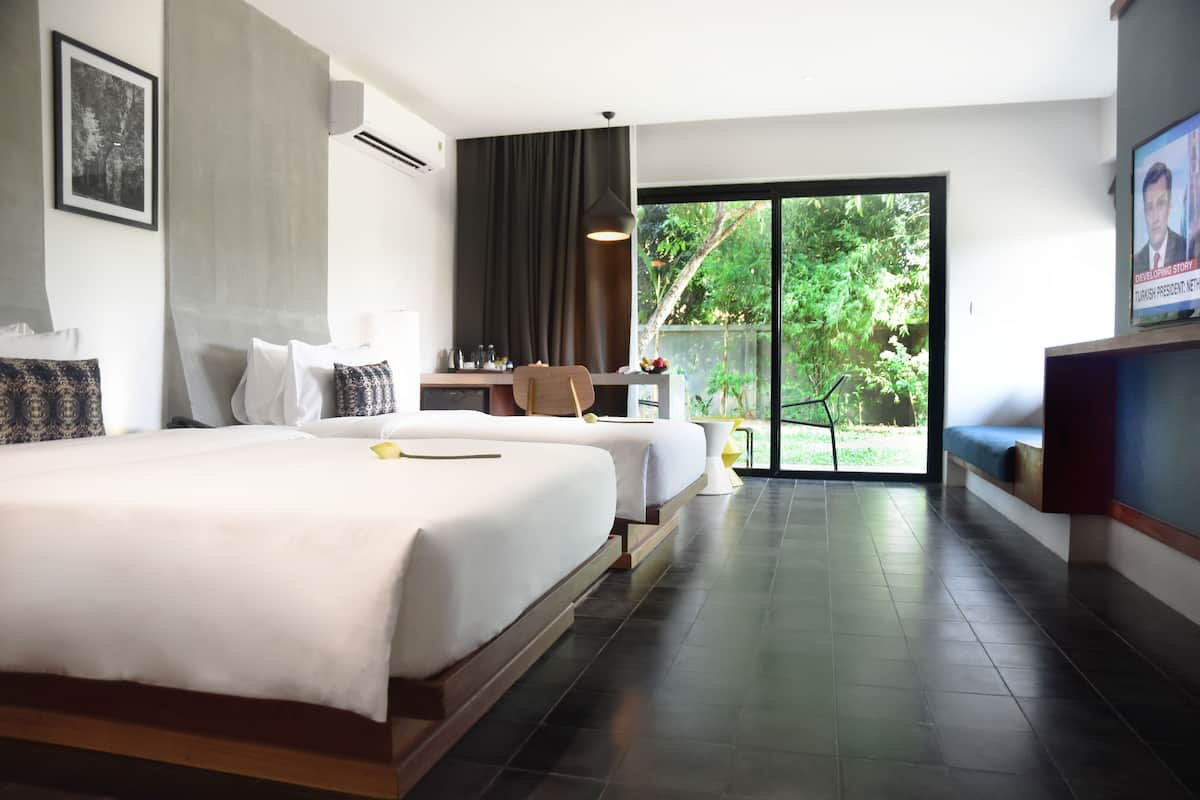 A hotel room with two beds, a desk, a chair, a TV, and a large sliding glass door leading to a balcony.
