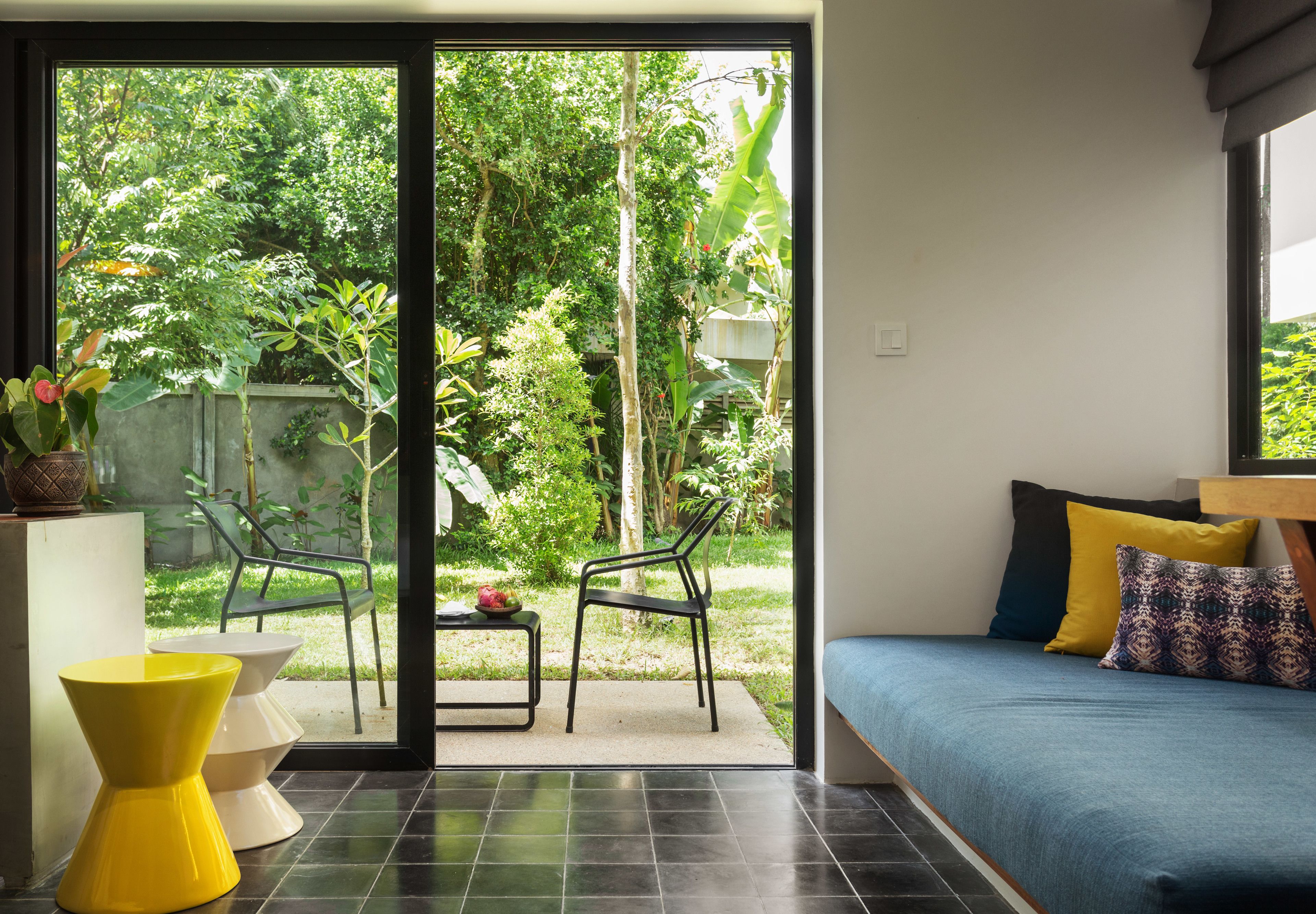 A room with a bed, a table with chairs, and a view of a garden through a glass door.