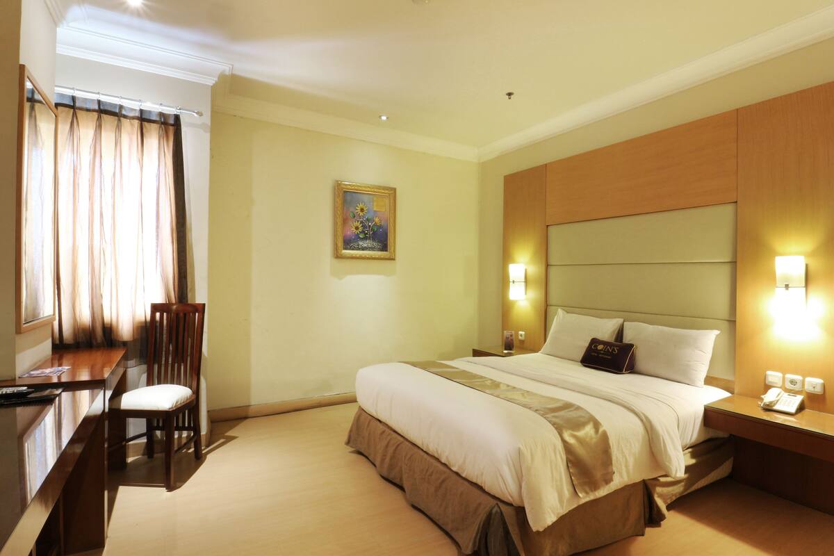 A hotel room with a bed, bedside table, lamp, and a desk with a chair.