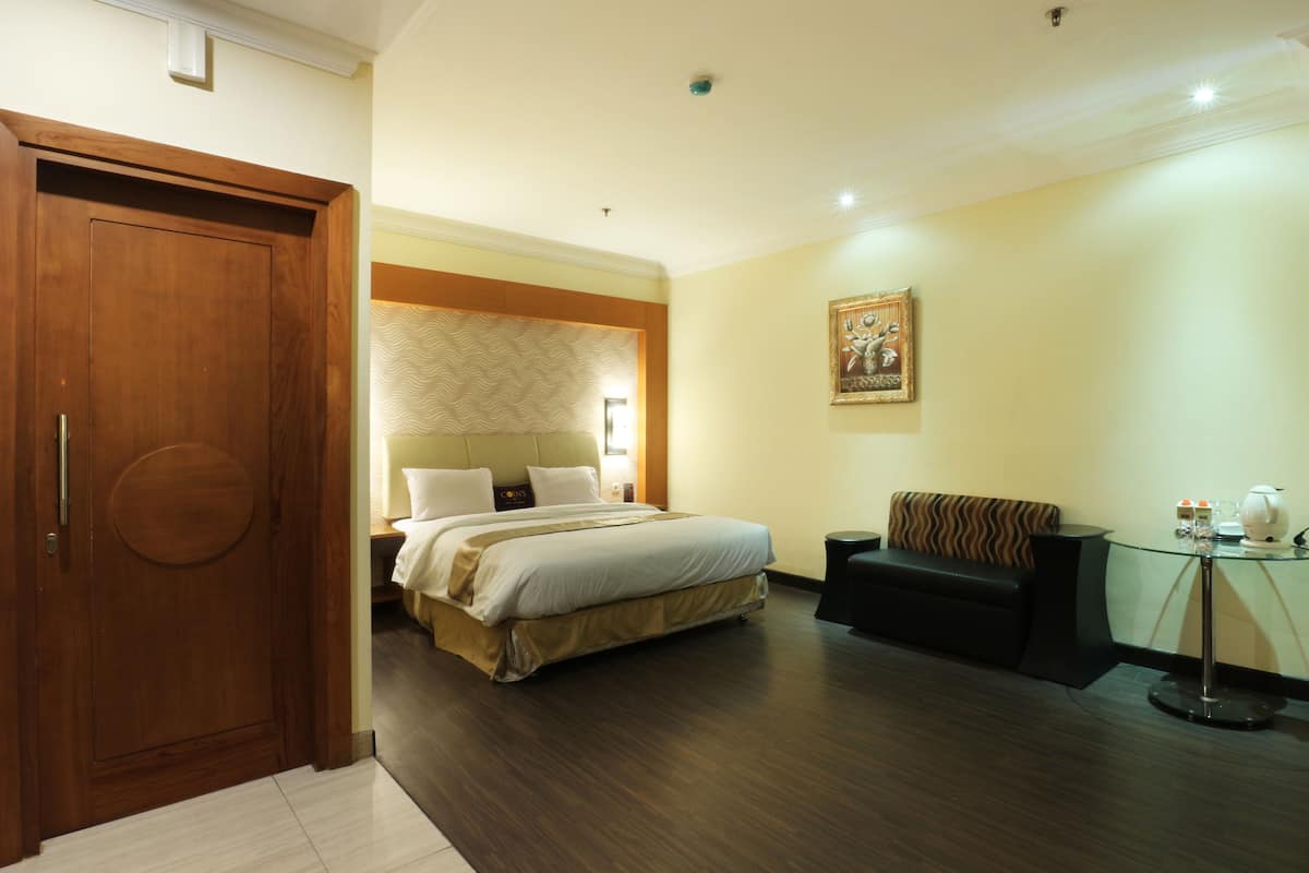 A hotel room with a large bed, a wooden wardrobe, a glass table, and a black sofa.