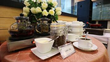 Een buffettafel met koffie en thee, een koffiezetapparaat en een vaas witte bloemen.