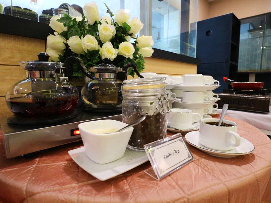 Een buffettafel met koffie en thee, een koffiezetapparaat en een vaas witte bloemen.
