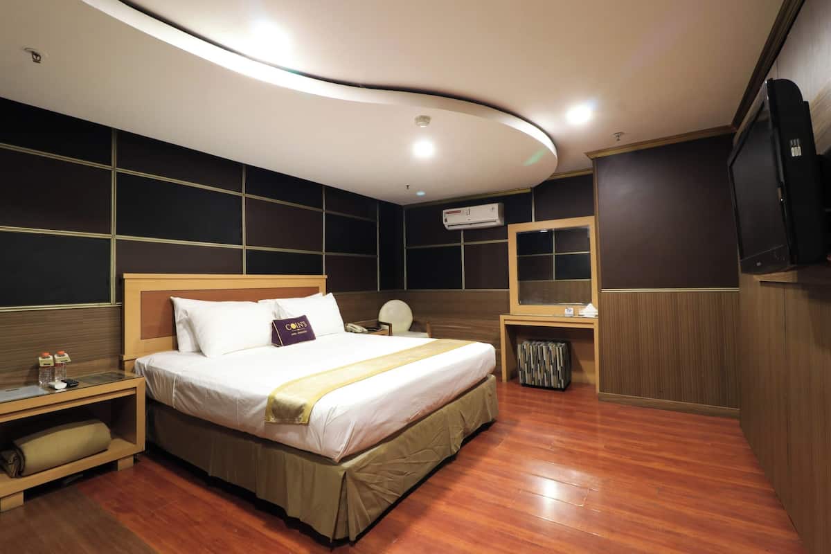 A modern hotel room with a large bed, bedside tables, a TV, and an air conditioning unit.