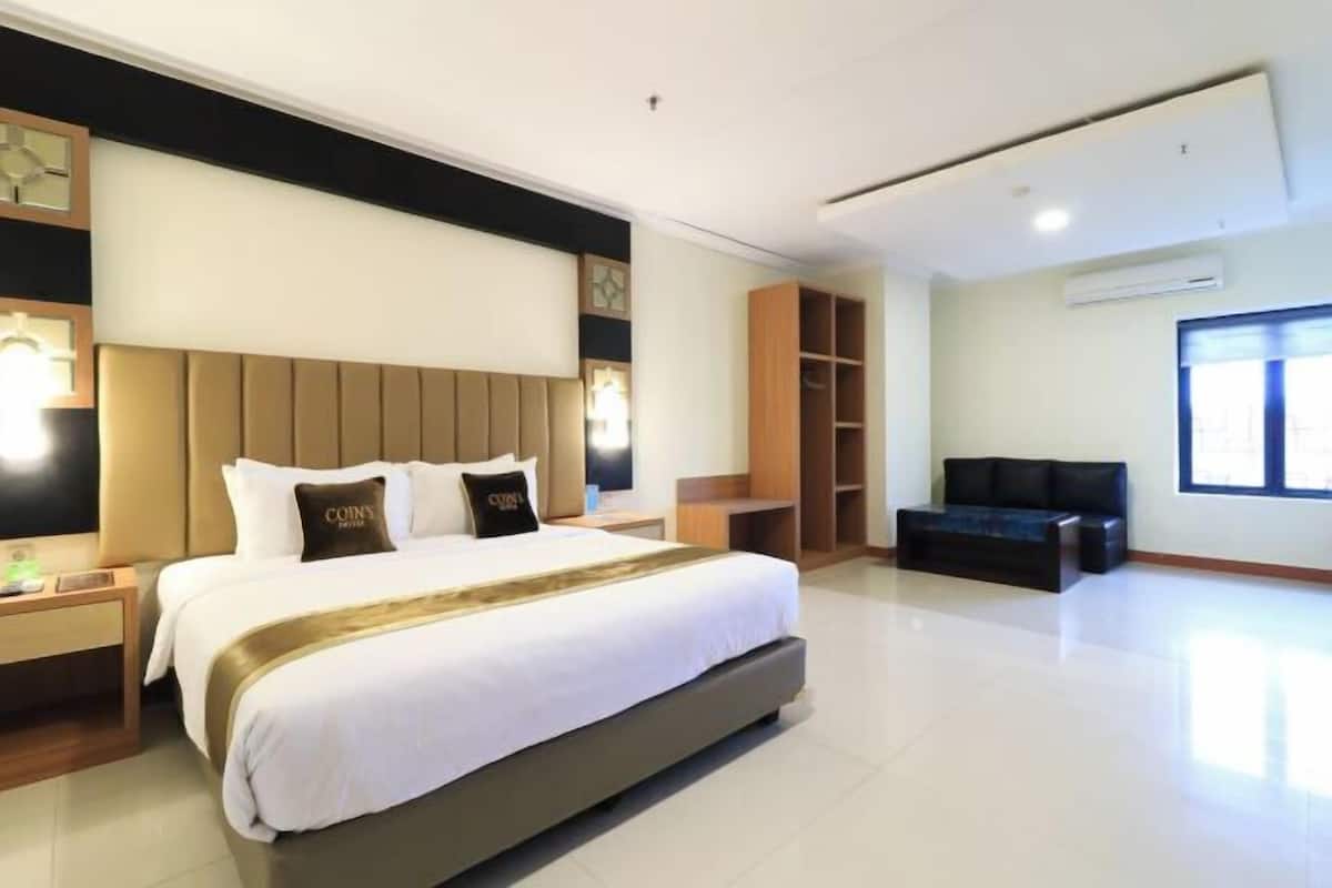 A hotel room with a large bed, bedside tables, a TV, a sofa, and a wardrobe.