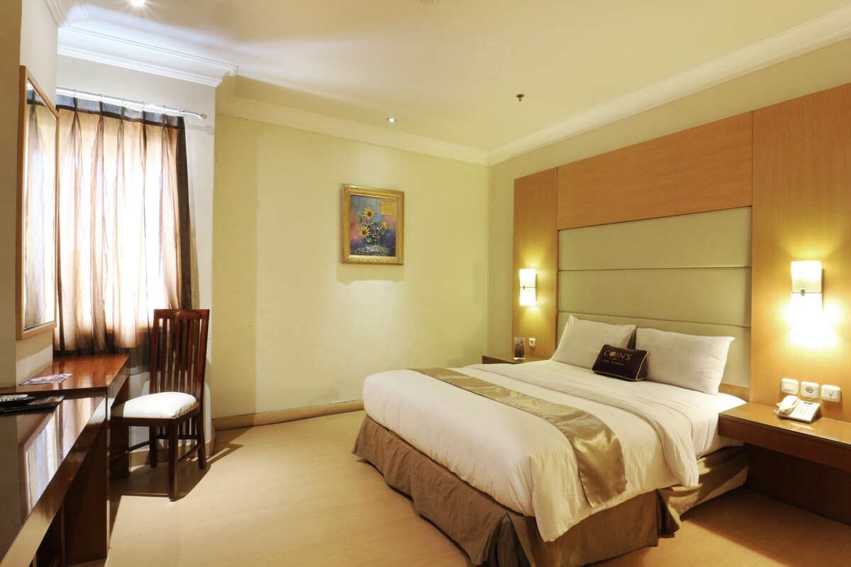 Habitación de hotel con cama, mesita de noche, lámpara y escritorio con silla.