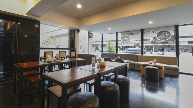Interior de una cafetería moderna con mesas de madera, otomanas de cuero negro y grandes ventanales con vistas a la calle.
