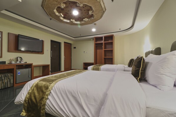 A hotel room with a large bed, a television mounted on the wall, a wardrobe, and a small desk with a refrigerator. - Coin's Hotel Jakarta (Jakarta)