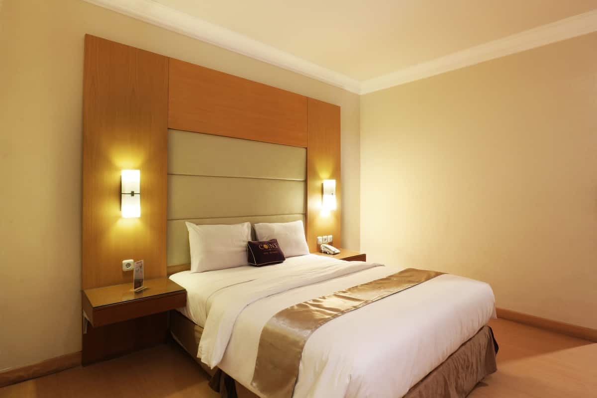 A hotel room with a large bed, wooden headboard, bedside lamps, and a nightstand with a phone.