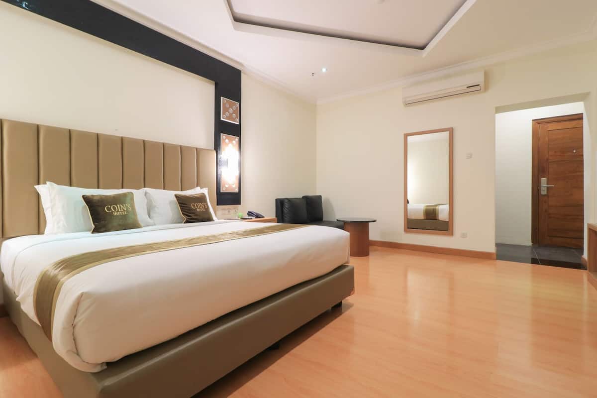A hotel room with a large bed, a headboard, a bedside table, a mirror, and a door.