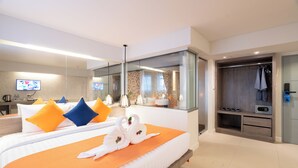 Ein modernes Hotelzimmer mit einem großen Bett, einem begehbaren Kleiderschrank, einem Badezimmer mit Glasdusche und einem an der Wand montierten Fernseher.