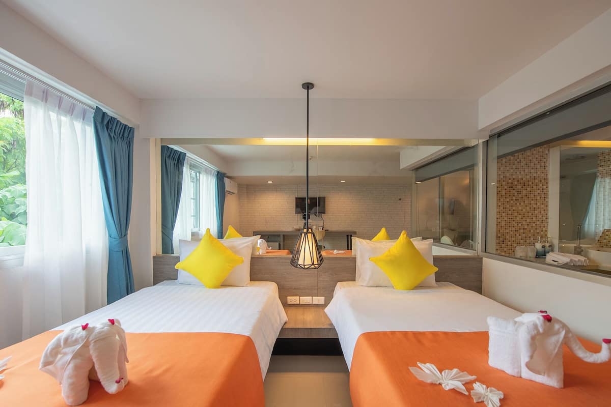 A hotel room with two beds, each with an orange bedspread and white pillows, a small elephant decoration, and a view of a kitchen area.