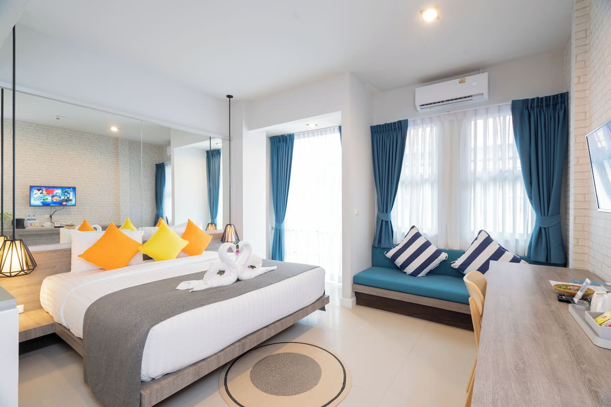 A modern hotel room with a large bed, a sofa, a dining area, and a TV.