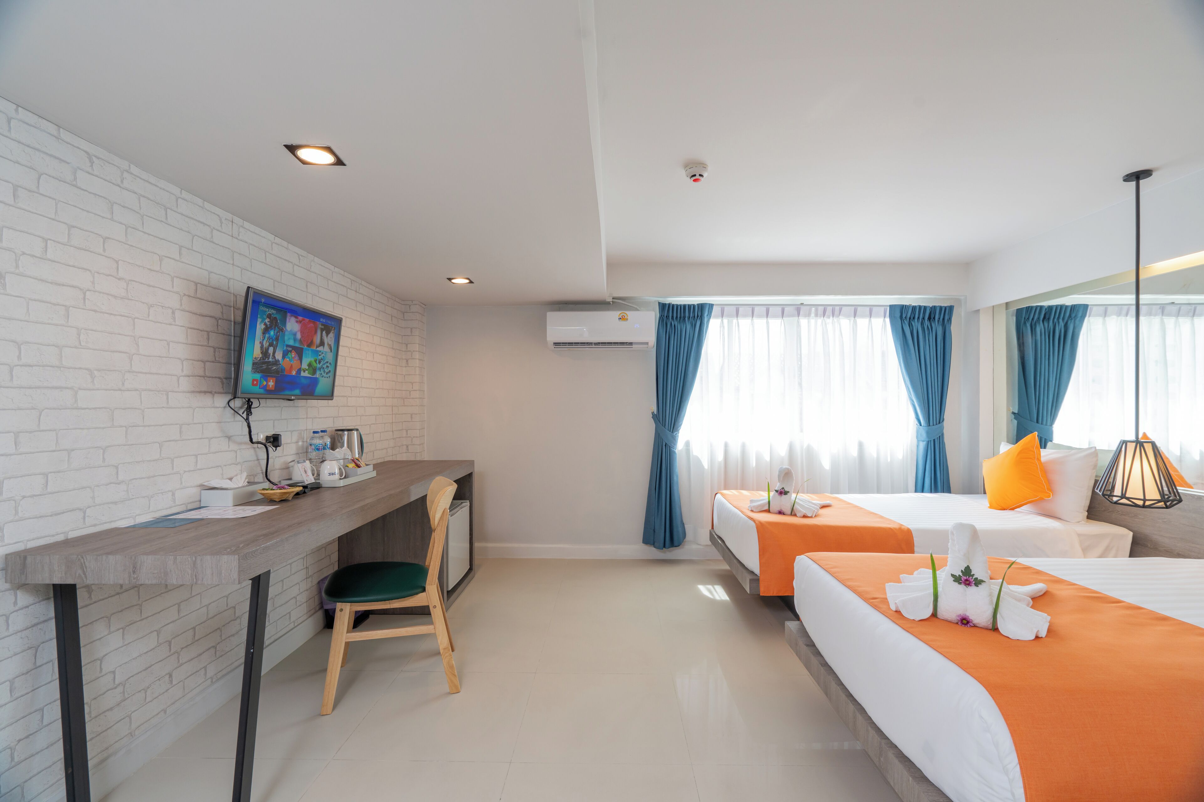 A hotel room with a desk, two beds, a TV, and a window with curtains.