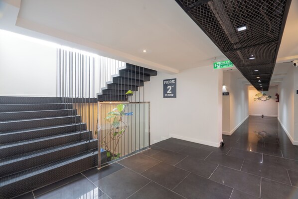 A modern interior with a staircase leading to the second floor, a fire exit sign, and a clean, tiled floor. - MORE Patong Hotel (Patong)