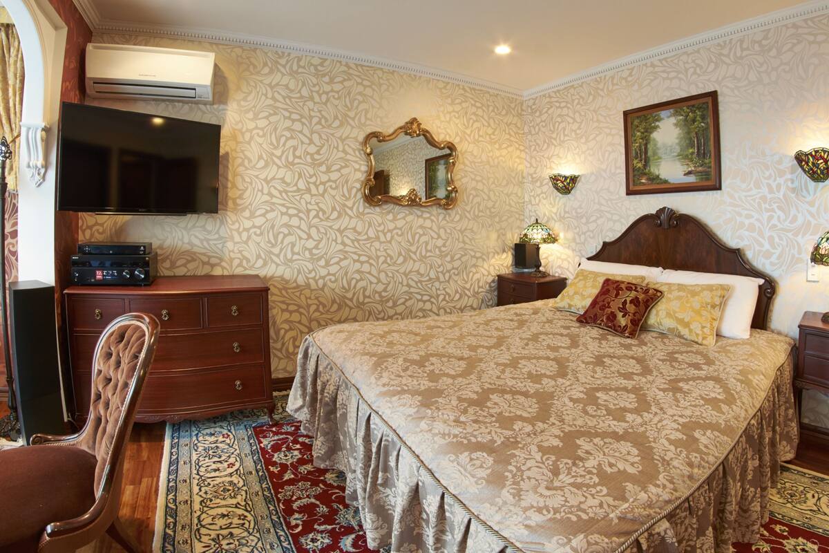 Un dormitorio bien amoblado con una cama grande, un aparador, una silla y un televisor.