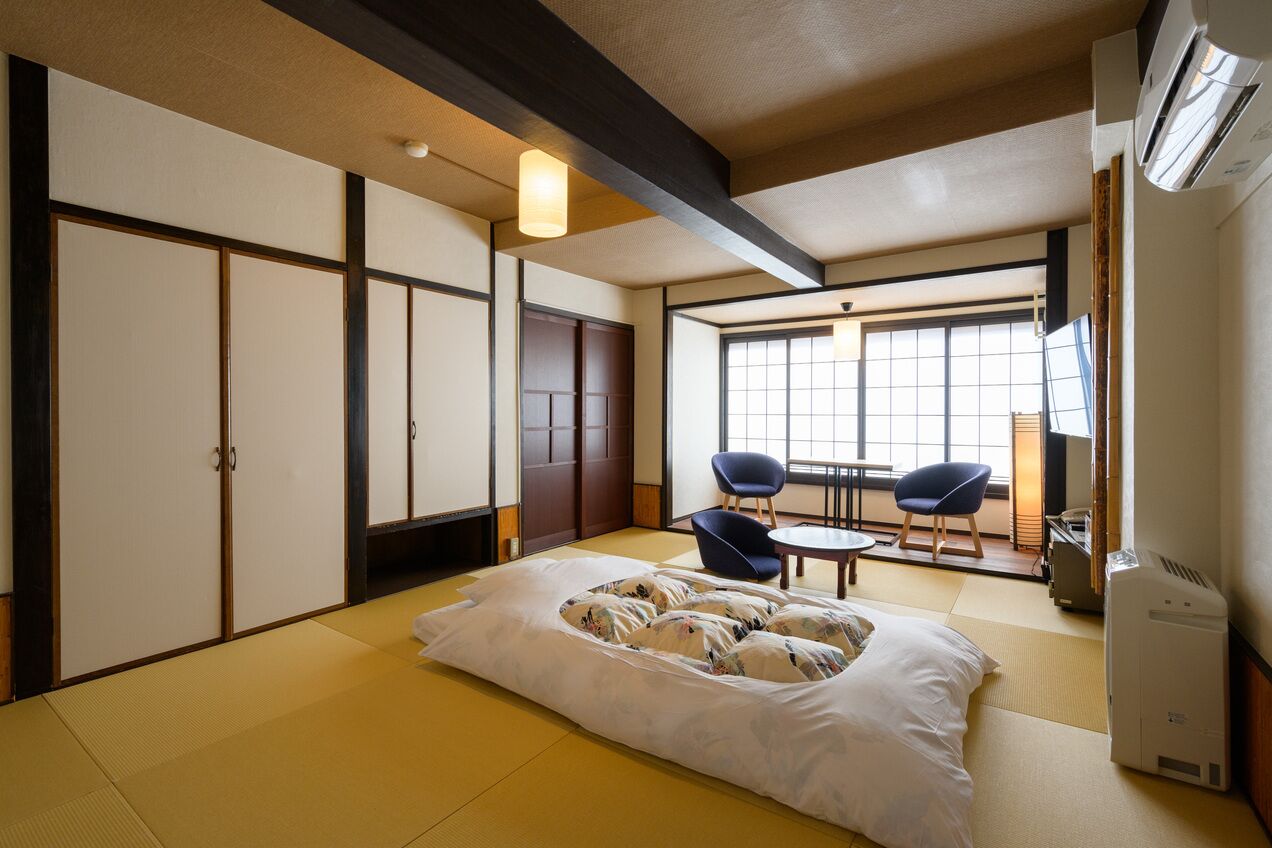A traditional Japanese room with tatami flooring, a futon bed, sliding doors, and a view of the outside.